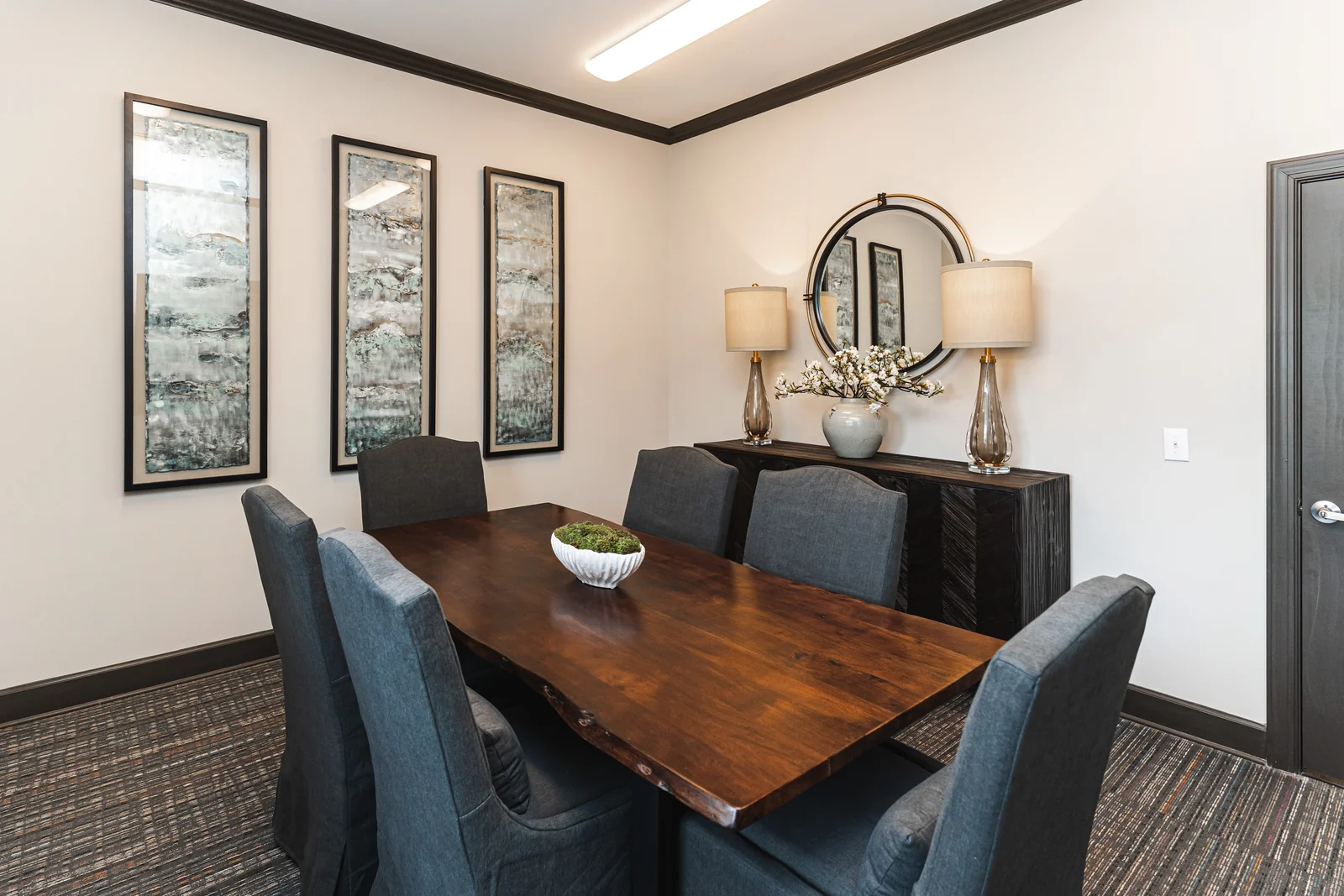 Commercial meeting room with a wood table, upholstered chairs, framed artwork, and a console