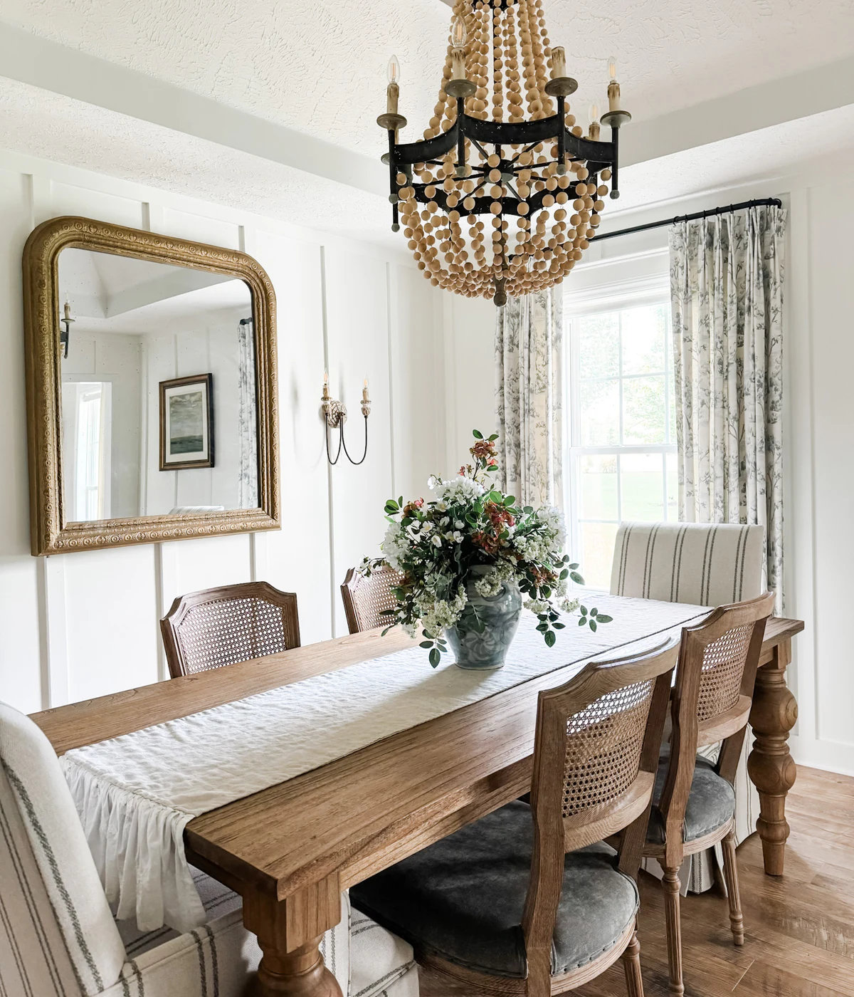Completed dining room with custom drapery, an antique mirror, and a beaded chandelier