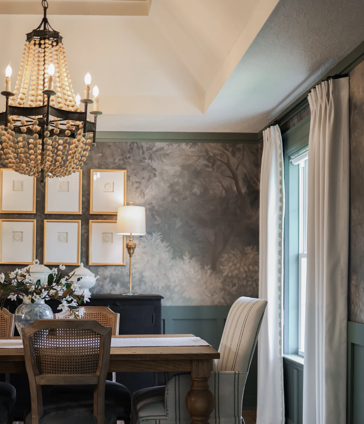 Completed dining room with full-length white drapery, botanical wallcovering, and a beaded chandelier